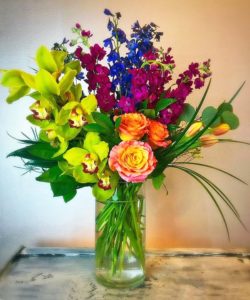 Beautiful green orchids,orange and yellow roses, and vibrant red and bluedelphinium make you dream of a tropical place on a relaxing beach!